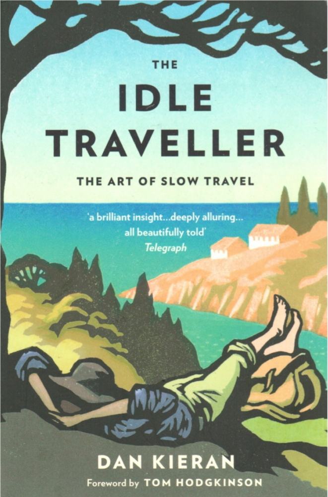 The Idle Traveller: The Art of Slow Travel by Dan Kieran, foreword by Tom Hodgkinson — book cover featuring a woodcut-style illustration of a person lying barefoot under a tree overlooking a coastal Mediterranean landscape